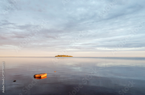 A tranquil evening by the calm sea with a small island and reflections on the water surface, Bothnian Bay, Baltic Sea, Finland