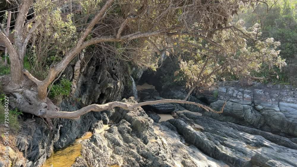 Mountain waterfalls flowing down the side onto the beach boulders Mountain waterfalls flowing down the side onto the beach boulders