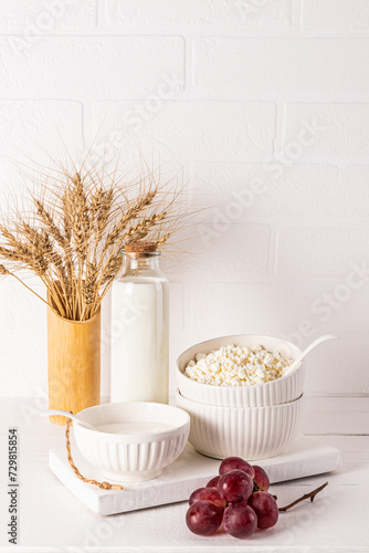 A beautiful still life for the holiday of Jewish Shavuot. Fresh dairy products  bunch of grapes and ears of bread on white vertical background.