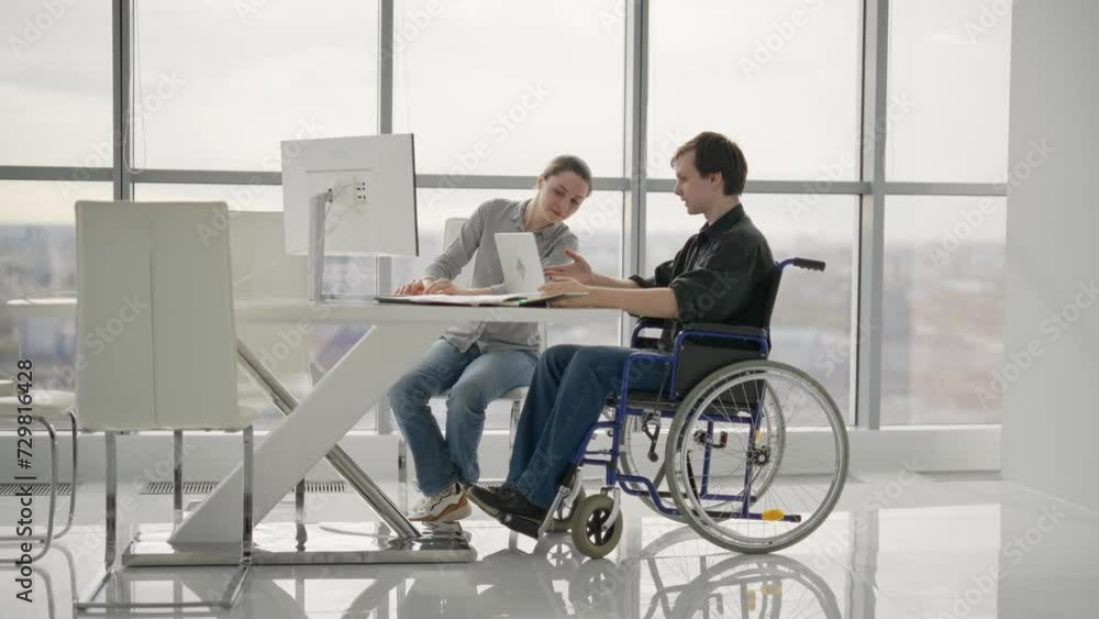Colleagues, woman shows to man in wheelchair pie chart on paper document work together in office. Workers discuss collect data sit at desk. Usual life of people with physical disability concept. Colleagues, woman shows to man in wheelchair pie chart on paper document work together in office. Workers discuss collect data sit at desk. Usual life of people with physical disability concept.