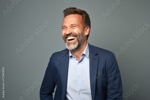 Handsome middle aged man laughing and looking at camera while standing against grey background