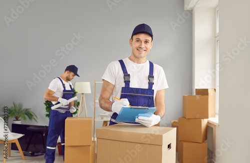 Young smiling mover man checking items list for moving, individual or company worker writing possessions, boxes, from one house to another, workman wearing uniform helping to change residence packing photo