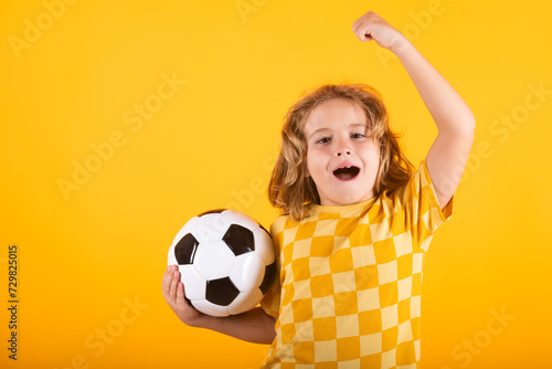 Kid holding soccer ball and smiling at camera, playing football, studio. Sport and leisure, soccer hobby for kids. Little boy holding soccer ball. Fan sport boy soccer player with football ball. © Volodymyr