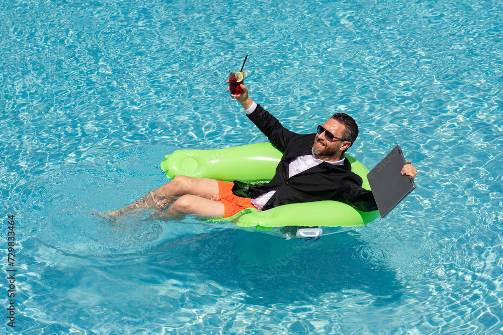 Business man in suit drink summer cocktail and using laptop in swimming pool. Travel business tourism. Office employee using laptop in pool on summer day. Successful businessman dreams in summer pool.