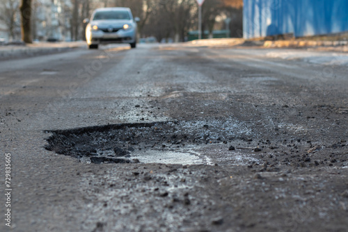 A pothole in the road and a car in the background that is moving towards this pothole
