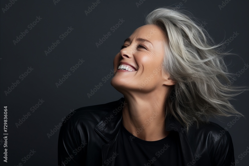 Happy mature woman with long blond hair smiling and looking up, on grey background