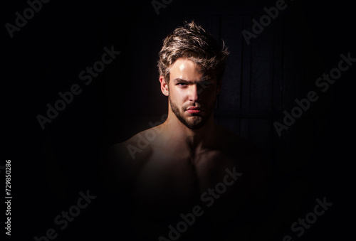 Attractive man face in shadow, looking at camera. Sexy man studio portrait. Handsome man in black studio portrait. Portrait of a young serious man at studio. High Fashion male model posing on black.