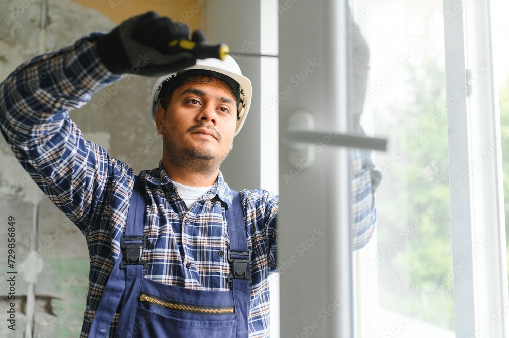Indian Workman in overalls installing or adjusting plastic windows in the living room at home Indian Workman in overalls installing or adjusting plastic windows in the living room at home