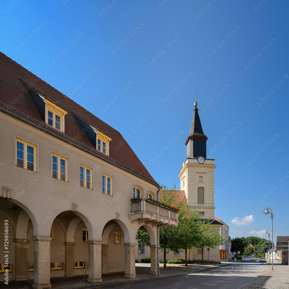 Das denkmalgeschützte Rathaus von Trebbin mit Säulengang und Balkon, dahinter die Stadtkirche 