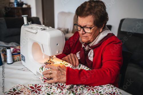 concentrated senior woman with glasses using sewing machine to sew a garment