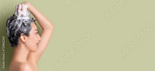 Asian woman applying shampoo on hair against green background with space for text photo