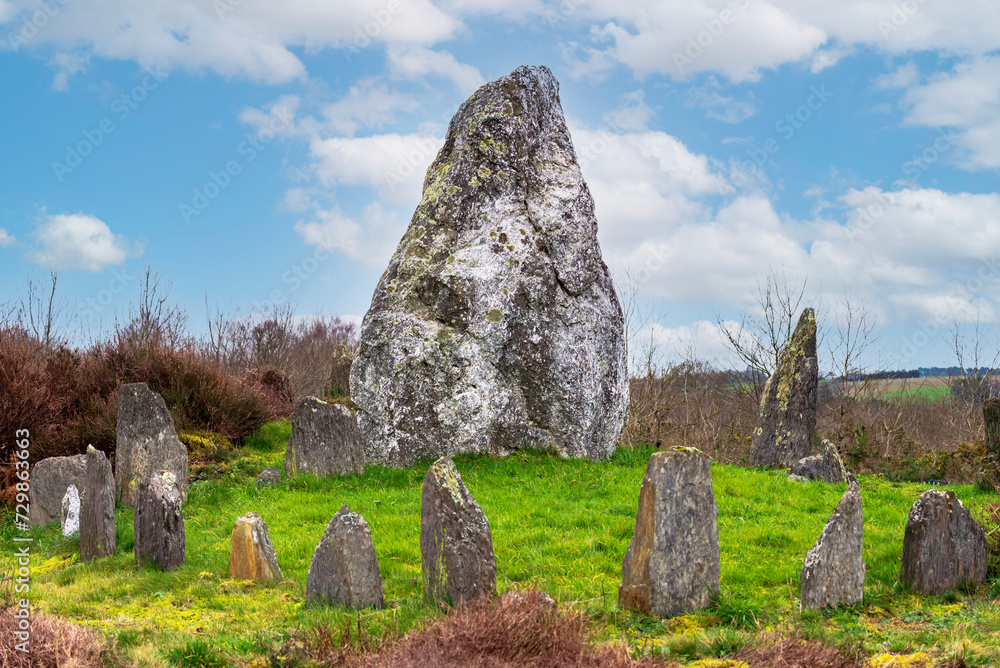 A large menhir surrounded by several small menhirs against a blue sky