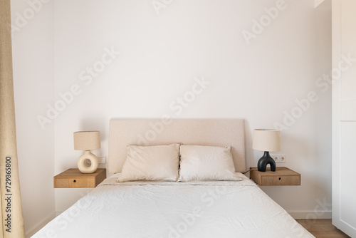 Horizontal shot of a double bed with white pillows and bedspread bedside tables sconces on a background of white wallpaper and a closet. Concept of a new apartment for a young family