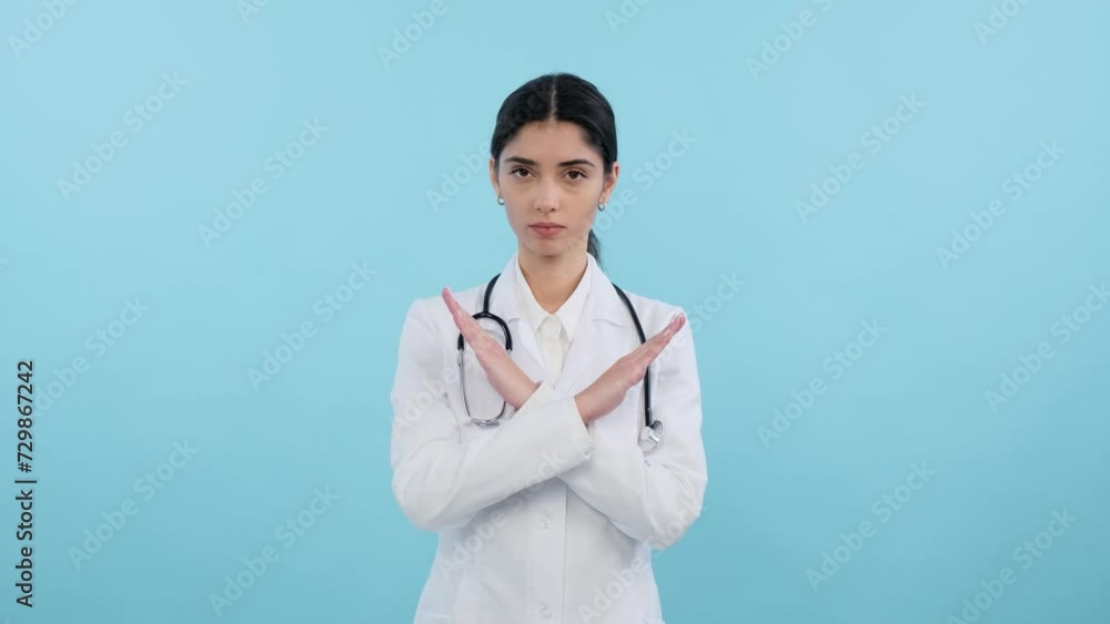 Serious doctor showing stop gesture with crossed arms and shaking head in disagreement or refusal on blue background. Negative and serious gesture of disapproval, restriction, denial. Serious doctor showing stop gesture with crossed arms and shaking head in disagreement or refusal on blue background. Negative and serious gesture of disapproval, restriction, denial.
