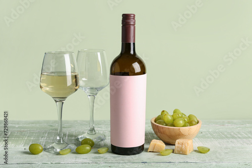 Glasses and bottle of tasty wine with blank label on green wooden table
