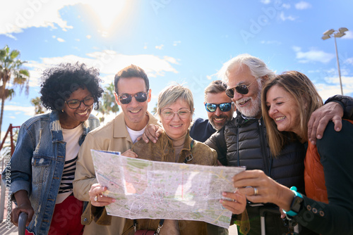 Group of diverse middle-aged tourist people standing looking at travel map in hands on street of vacation city happy and smiling on sunny day. Adults friends in community enjoying a trip together  photo