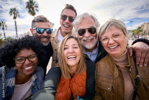 Group of diverse cheerful middle-aged tourist friends posing smiling taking a photo selfie embracing together with front camera on travel outdoor. Mature happy six people enjoy holidays sunny day  photo