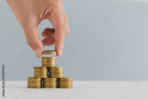 For financial pyramid, business growth, saving money, RMF, LTF, fund concept. Hand put more coin on top of  coins stacking in pyramid shape, including copy space photo