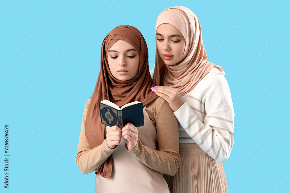 Fototapeta premium Young Muslim women in hijab with Koran on blue background