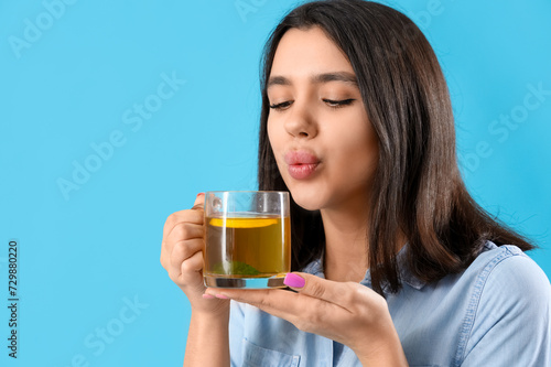Young woman with glass cup of hot lemon tea on blue background, closeup