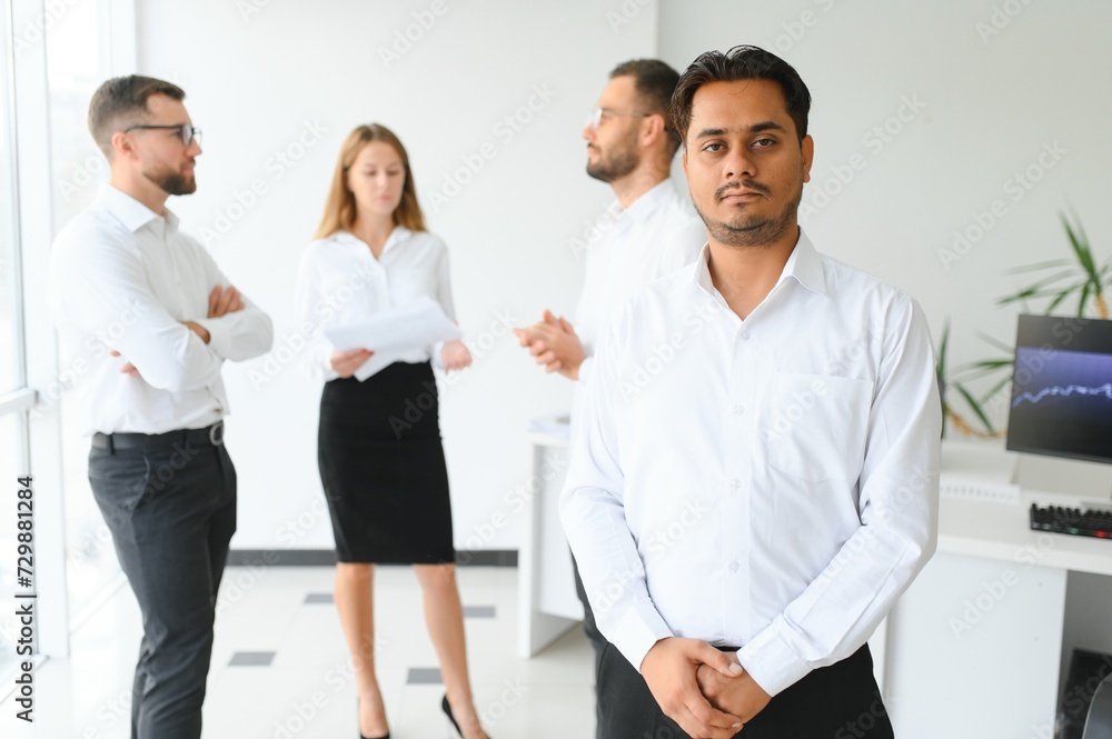 Portrait of smiling indian businessman standing in modern office on colleagues background Portrait of smiling indian businessman standing in modern office on colleagues background