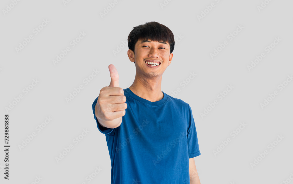 Happy young man in blue t-shirt with a smile pointing thumbs up isolated on gray background. Well done. Agreement concept. Happy young man in blue t-shirt with a smile pointing thumbs up isolated on gray background. Well done. Agreement concept.