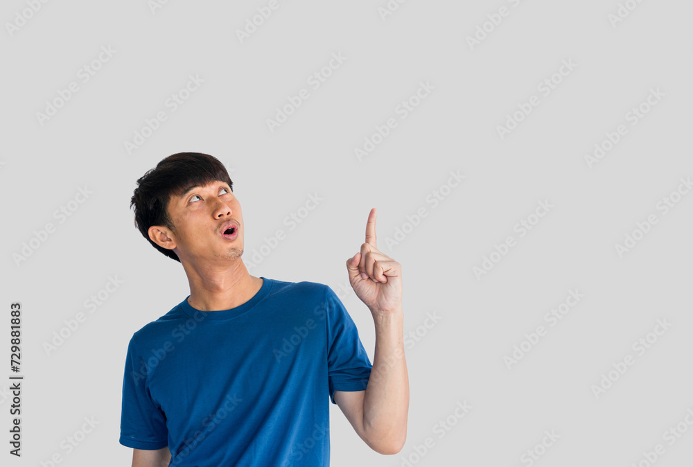 Shocked face of Asian man in blue shirt isolated on gray background. Person's index finger pointing to blank space for text Shocked face of Asian man in blue shirt isolated on gray background. Person's index finger pointing to blank space for text