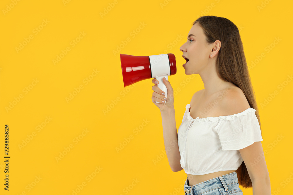 Attractive young girl stands on a yellow background with a loudspeaker Attractive young girl stands on a yellow background with a loudspeaker
