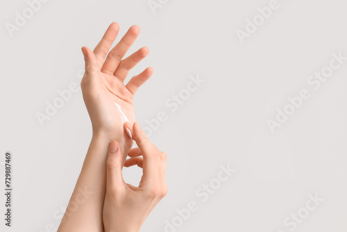 Woman applying cream onto her hands against light background  closeup