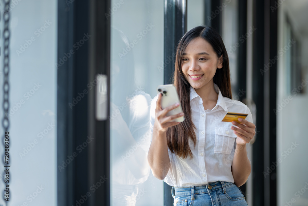 Smiling young woman using smartphone and holding credit card, potentially making an online purchase.. Smiling young woman using smartphone and holding credit card, potentially making an online purchase..