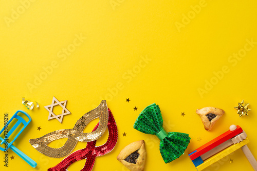 Joyous Purim theme captured from top view, showcasing iconic hamantaschen cookies, Star of David, celebratory accessories like masks, bow tie, ratchets on vibrant yellow backdrop for your message photo