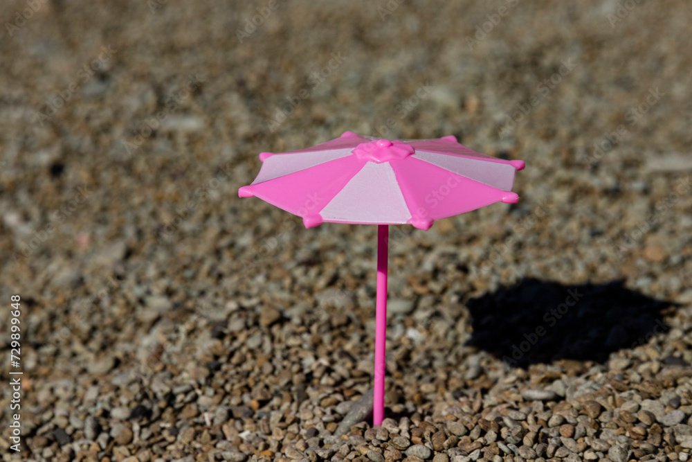 Toy umbrella with a shadow from the sun on a rocky beach, seashore. The concept of a place under the sun. Toy umbrella with a shadow from the sun on a rocky beach, seashore. The concept of a place under the sun.