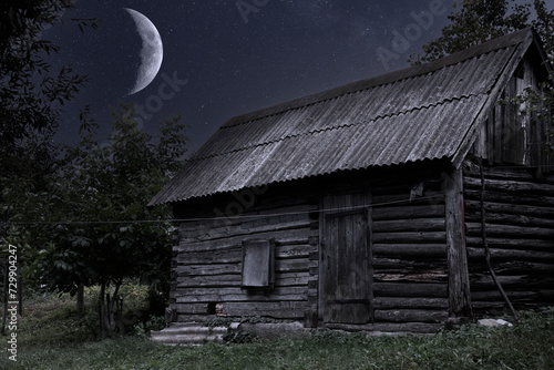 A growing, young moon in the night sky with stars and a lonely rustic old house made of wooden logs. Fairy night. Card.
