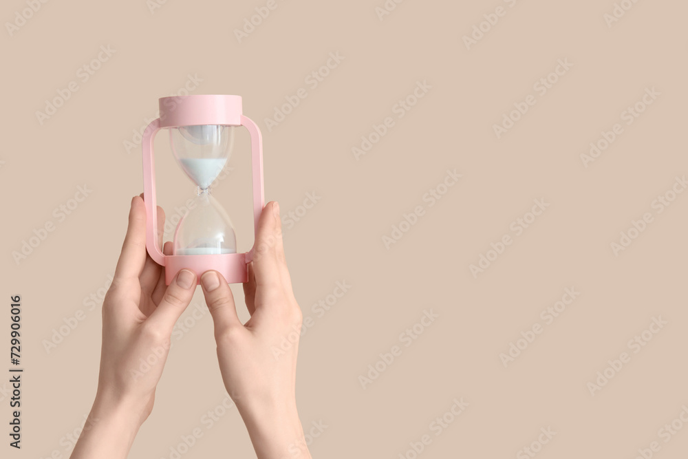 Female hands holding hourglass on beige background Female hands holding hourglass on beige background