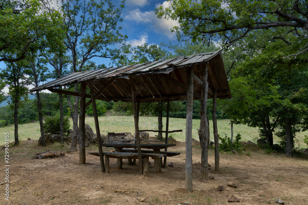 An equipped resting place for a picnic in the mountains, wooden benches and a table under the roof against the backdrop of a mountain landscape.