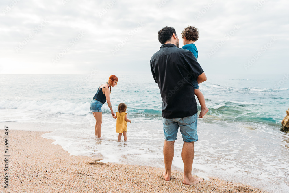Family standing on seashore near waving seawater