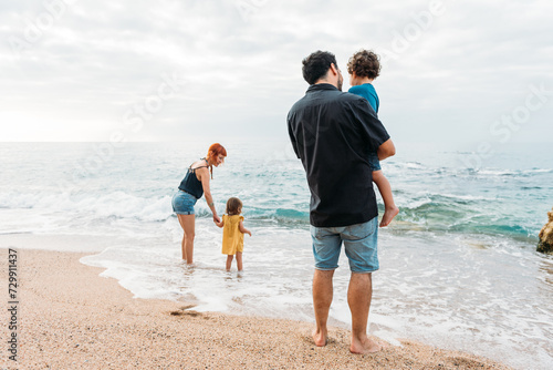 Family standing on seashore near waving seawater