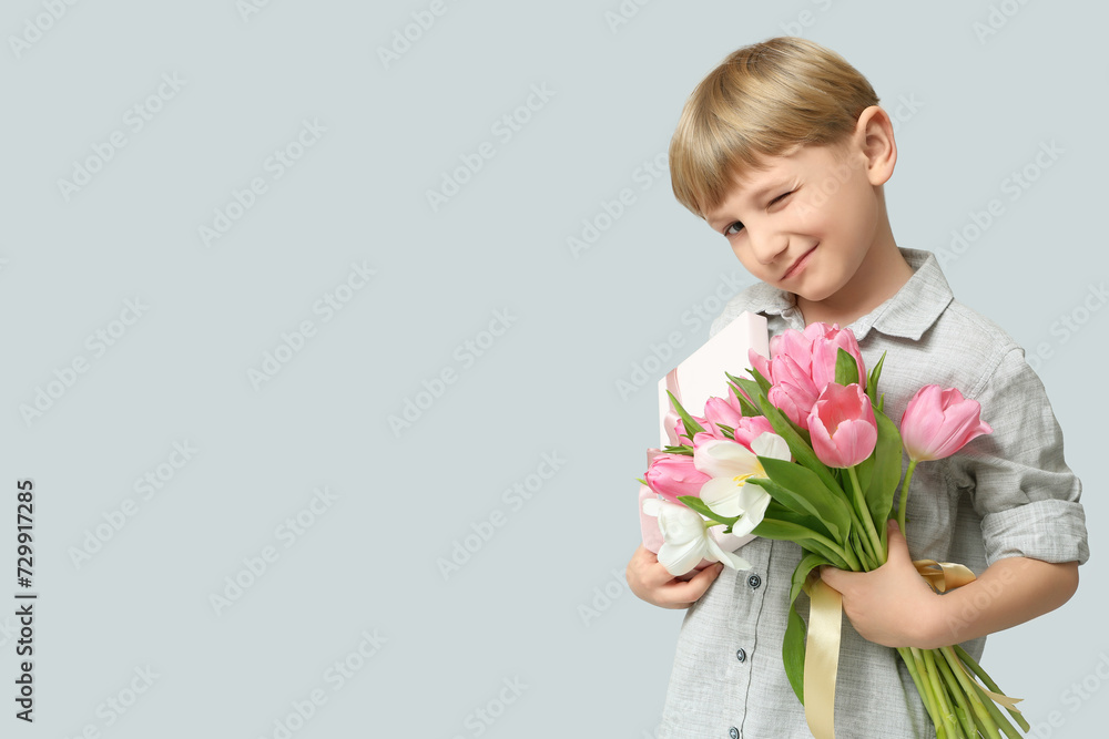 Cute little boy with bouquet of beautiful tulips and gift box on grey background. International Women's Day