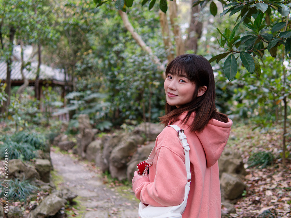 Beautiful young Chinese woman smiling and looking back, wearing pink loose oversized top with small white shoulder bag. Candid moment. Emotions, people, beauty, youth and lifestyle portrait. Beautiful young Chinese woman smiling and looking back, wearing pink loose oversized top with small white shoulder bag. Candid moment. Emotions, people, beauty, youth and lifestyle portrait.
