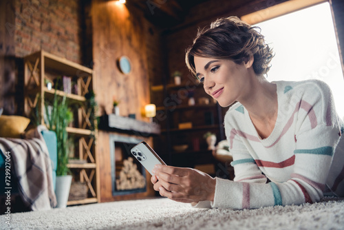 Profile photo of lovely girl lying carpet floor use smart phone enjoy pastime harmony apartment indoors