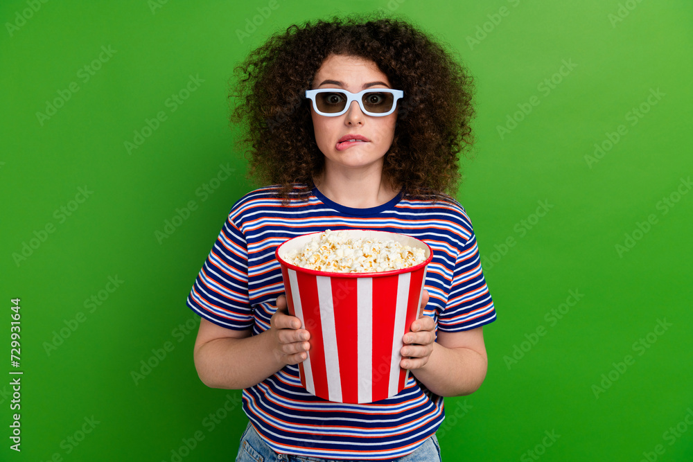 Portrait of worried person arms hold pop corn bucket biting lips watch movie 3d glasses isolated on green color background Portrait of worried person arms hold pop corn bucket biting lips watch movie 3d glasses isolated on green color background