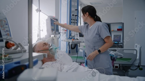 Emergency room with modern equipment in clinic. Senior man in oxygen mask lies in bed during lung ventilation. Friendly nurse adjusts life support machine for old patient. Intensive care department.