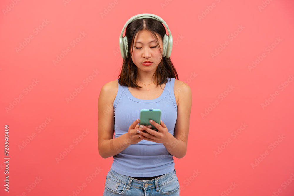 Portrait of angry girl looking at mobile phone, serious, texting on pink background. Concept of human emotions, facial expression. Copy space for your ad Portrait of angry girl looking at mobile phone, serious, texting on pink background. Concept of human emotions, facial expression. Copy space for your ad