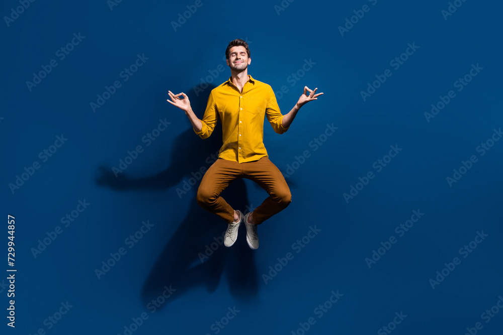 Obraz premium Full size photo of attractive young man jumping meditate closed eyes dressed stylish yellow clothes isolated on dark blue color background