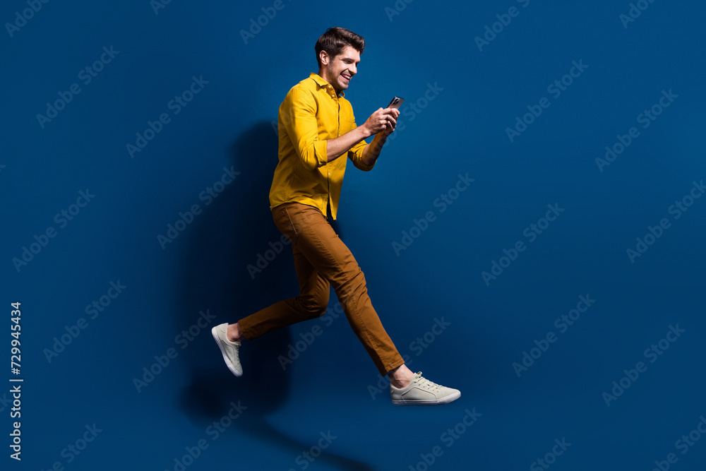 Full length photo of nice young male running hold telephone dressed stylish yellow garment isolated on dark blue color background