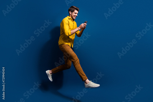 Full length photo of nice young male running hold telephone dressed stylish yellow garment isolated on dark blue color background © deagreez