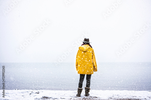 Solo  traveler with yellow rain coat and cowbow hat lookng away under snow, back shot photo