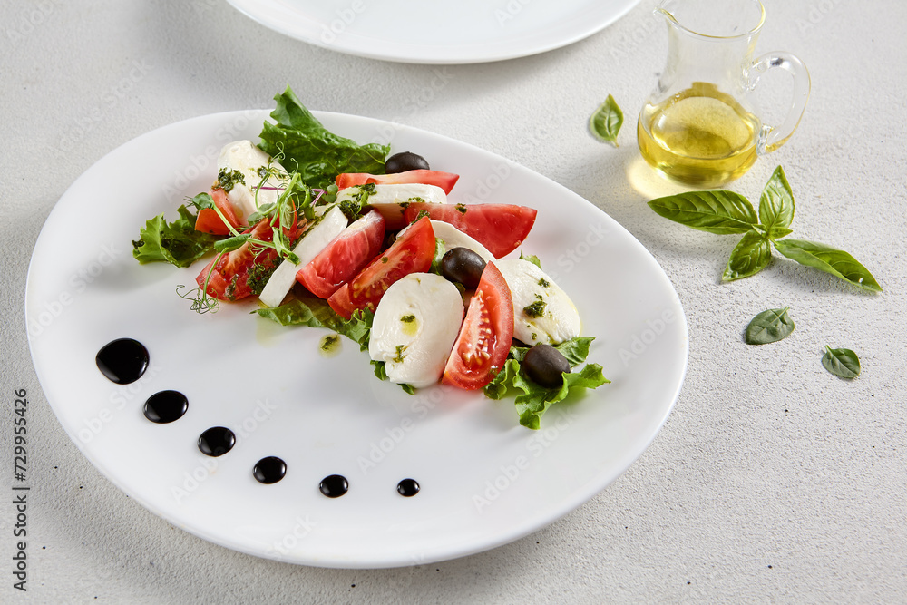 Classic Caprese salad with ripe tomatoes, mozzarella, and olives, garnished with fresh basil. Suitable for Italian cuisine promotions and cookbooks Classic Caprese salad with ripe tomatoes, mozzarella, and olives, garnished with fresh basil. Suitable for Italian cuisine promotions and cookbooks