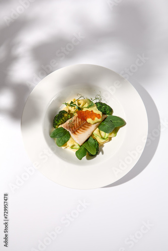 Grilled cod fillet with caviar and a side of zucchini and broccoli, top view on white with elegant shadow detailing