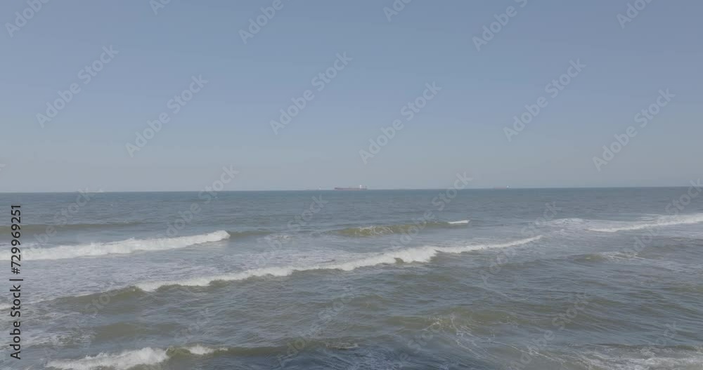 Gentle waves lapping at the shore with a distant cargo ship on the horizon, clear blue sky Gentle waves lapping at the shore with a distant cargo ship on the horizon, clear blue sky